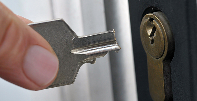 a person holding up a snapped key next to a lock of a front door