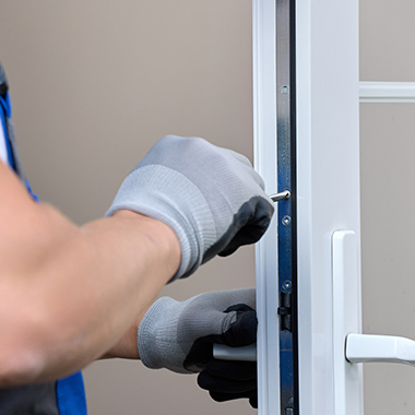 a locksmith with gloves on finishing the installation of a lock on a white framed glass door