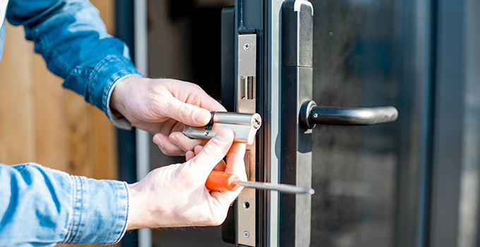 a person with a screwdriver replacing the lock on an outdoors glass door