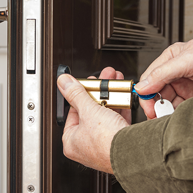 a locksmith replacing a lock cylinder on a varnished dark wooden door