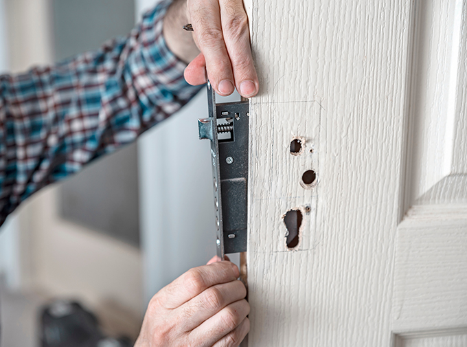 a locksmith replacing the inner lock mechanism on a wooden door painted white