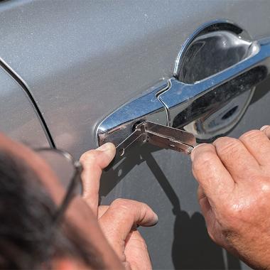 A person using a specialist tool to unlock silver car